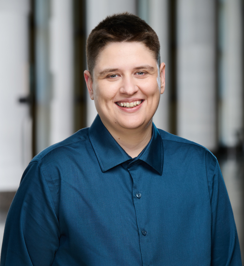 Light-skinned smiling adult with short brown hair and a blue dress shirt.