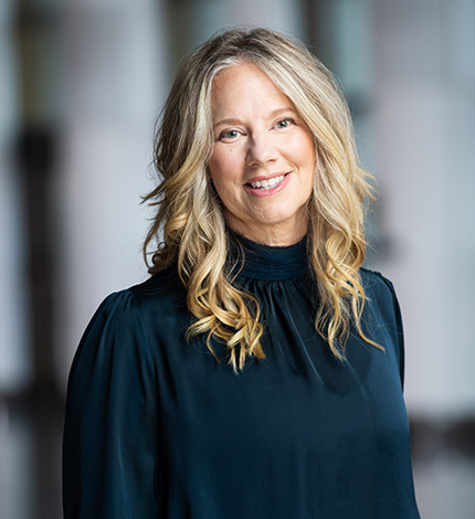 Light-skinned smiling adult with long wavy blonde hair and a dark blue top.