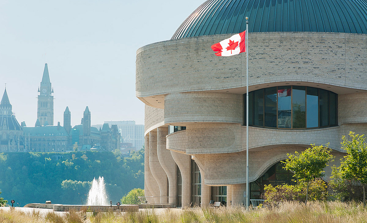 A large building with curved stone walls and columns, and dark green metal domes on the roof.