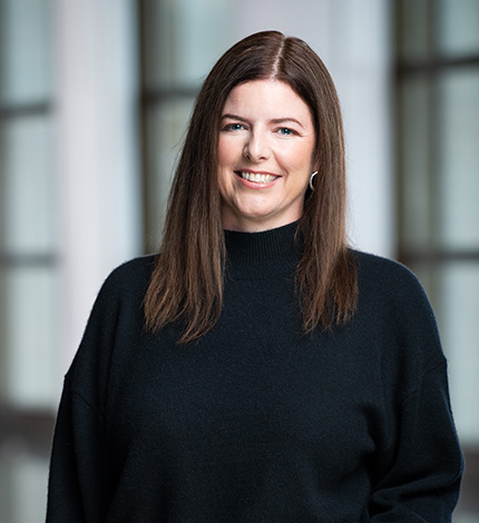 Light-skinned smiling adult with long, straightbrown hair, silver and black earrings, and a black blazer and blouse.